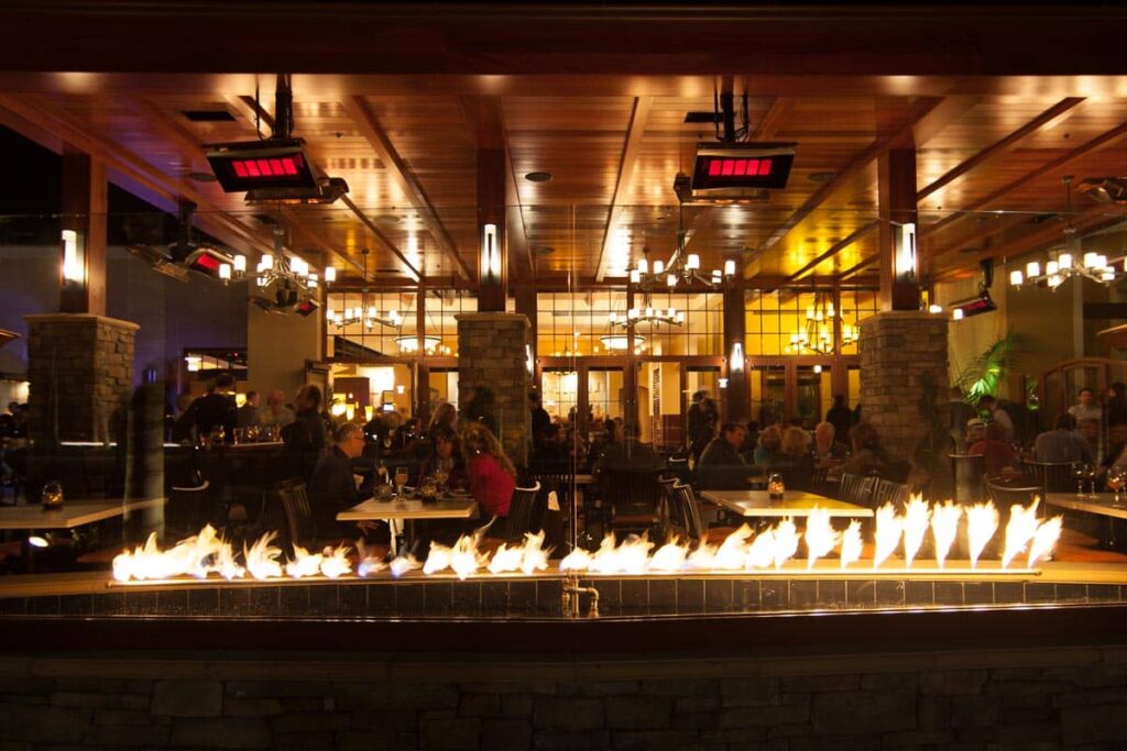 bustling and dimly lit restaurant with fire countertop feature and gas heaters
