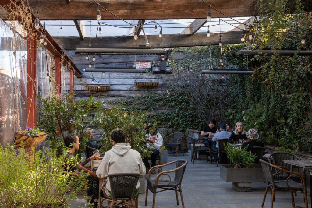 Busy outdoor cafe with electric heaters and an abundance of plant life and string lighting